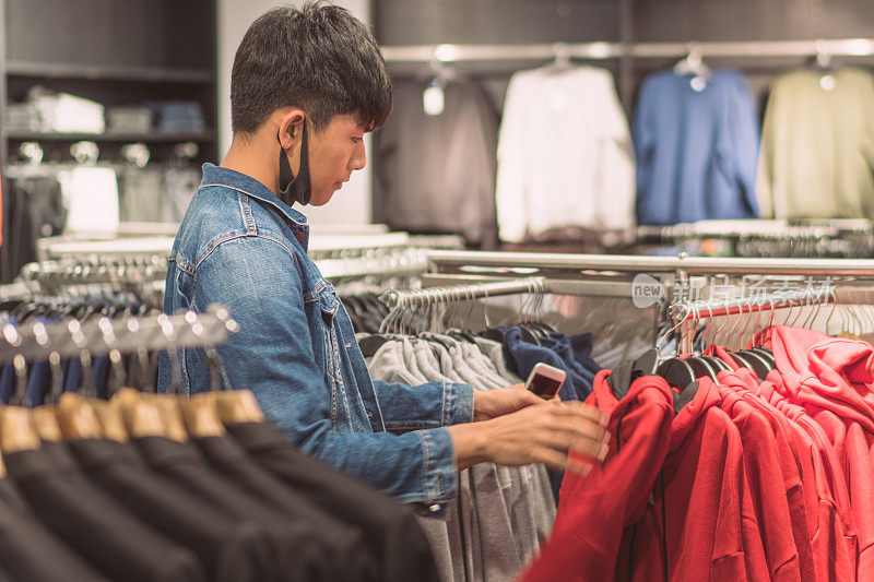 快乐的年轻亚洲男人在购物中心或服装店选择夹克