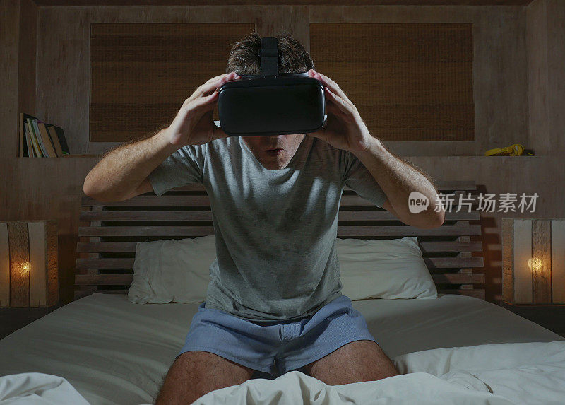 年轻兴奋和惊奇的男人戴着VR虚拟现实眼镜设备玩互联网3D模拟游戏，享受刺激和震撼的视觉体验在家里的床上
