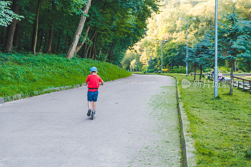 一个小孩骑着滑板车经过城市公园