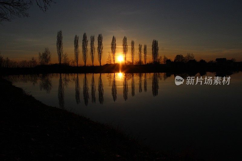 夕阳西下，树木倒映在湖面上