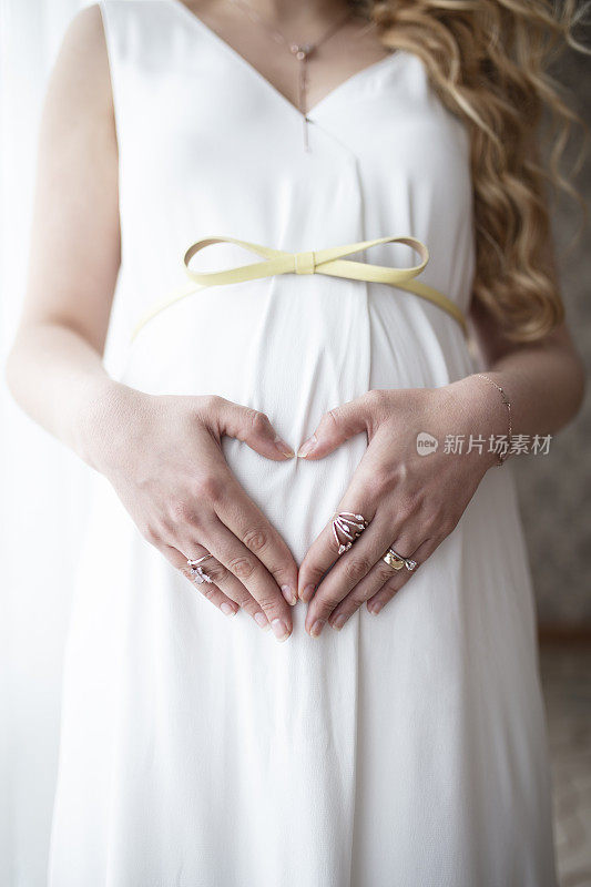 一名孕妇将手放在肚子上做一个心形的符号