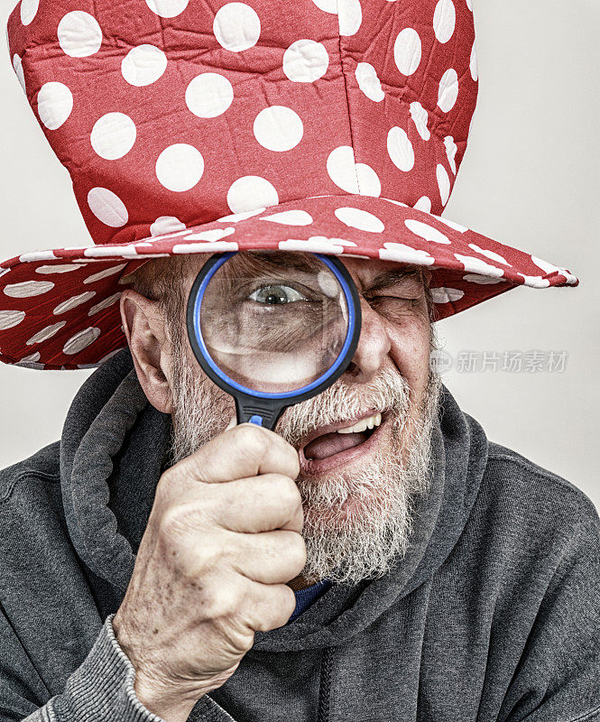 好奇的圆点小丑大礼帽老男人透过放大镜凝视