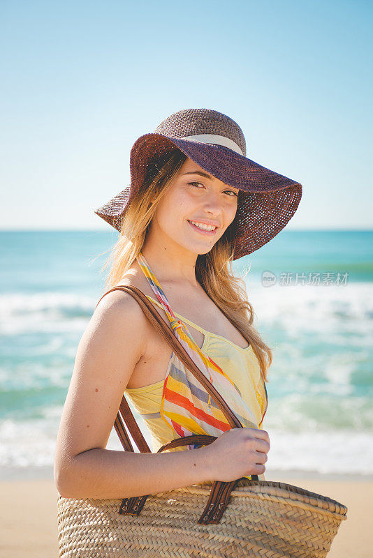 面带微笑的美丽女孩戴着草帽走在海滩上