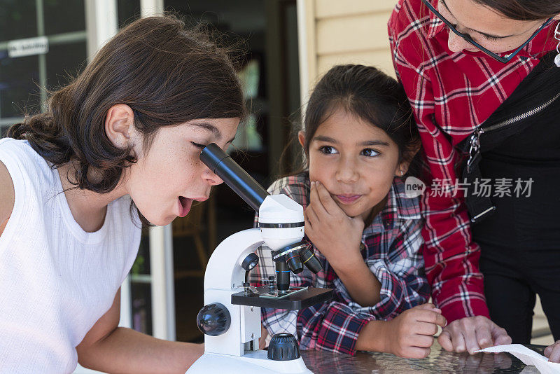 小男孩和小女孩在他17岁的姐姐的监督下使用显微镜