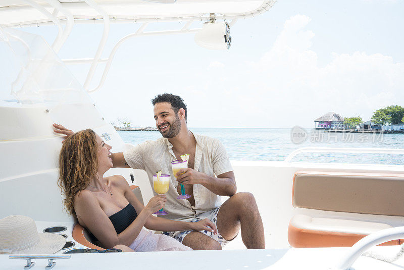一对拉丁裔夫妇坐在海中央的游艇上，微笑着喝着鸡尾酒