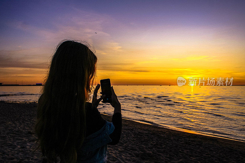 女人在旅行，用智能手机拍摄日落时美丽的海景