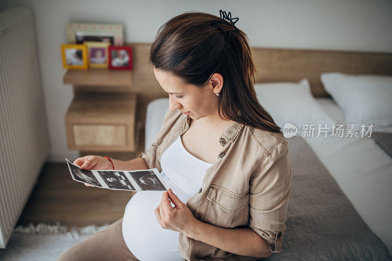 一名孕妇独自坐在卧室的床上看超声波扫描