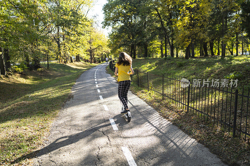 那个女孩在公园的小巷里推着滑板车往前走