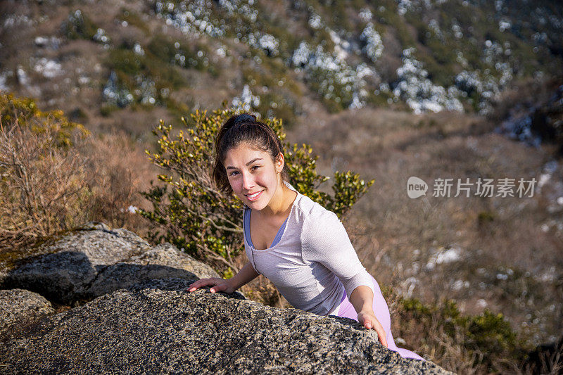 年轻女子攀登岩石到山顶的肖像