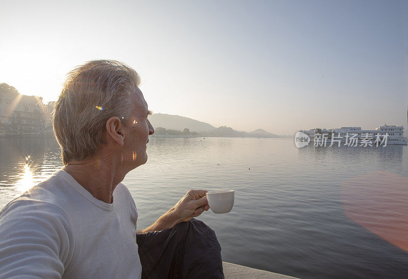 成熟的男人拿着茶杯，倾身眺望湖面