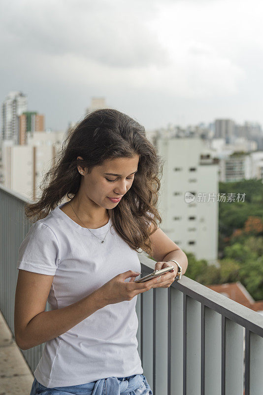 一名年轻的巴西女子在阳台上，用手机点击和发短信