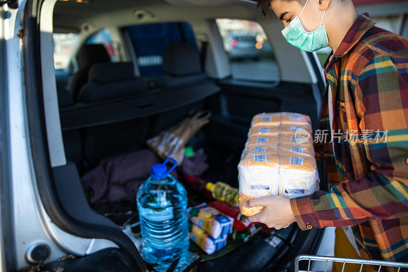 一名十几岁的男孩在冠状病毒大流行期间往汽车后备箱装食物