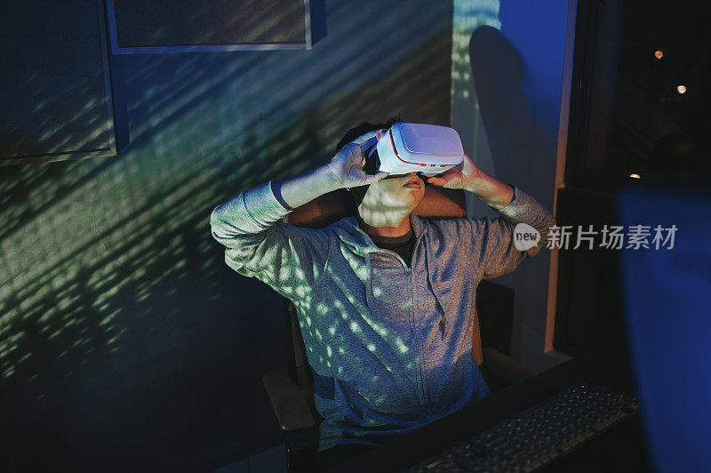 一名亚裔中国男性，晚上在他的家庭办公室自习室，戴上VR眼镜，在他的台式电脑前体验3D虚拟游戏