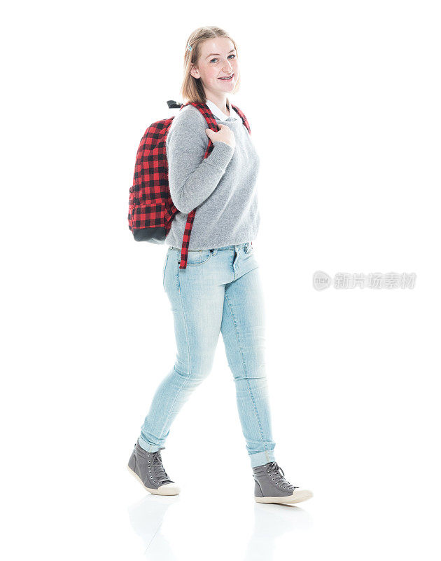 z一代的少女高中生穿着毛衣拿着包走在白色背景前