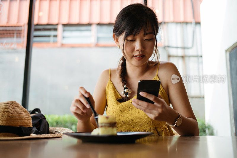年轻女性亚洲游客休息和有一片芝士蛋糕在咖啡馆