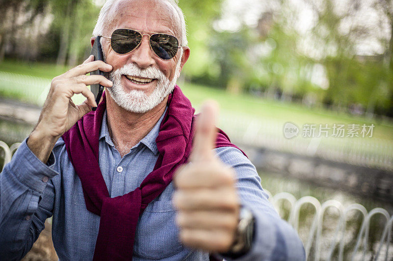 老人愉快地讲电话，笑出声来——一个老人正在户外讲手机