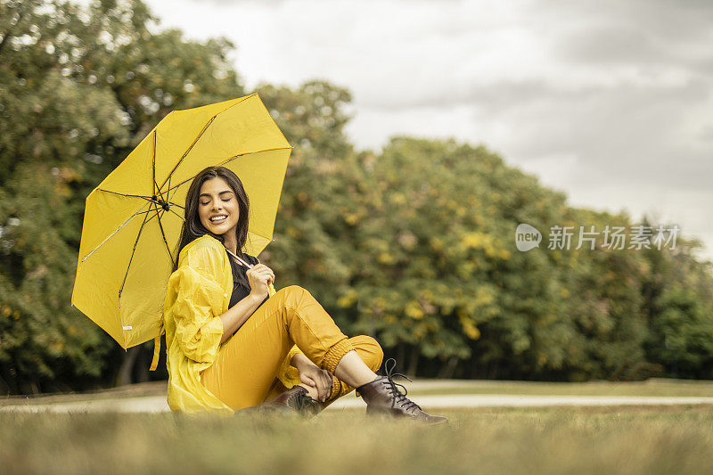 美丽的年轻女子穿着黄色雨衣，拿着黄色雨伞在户外