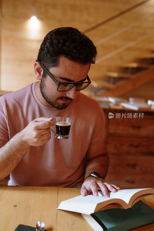 一个年轻人一边在自助餐厅喝咖啡，一边看书