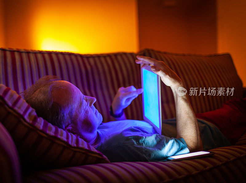 晚上，男人躺在沙发上，用平板电脑发出蓝光