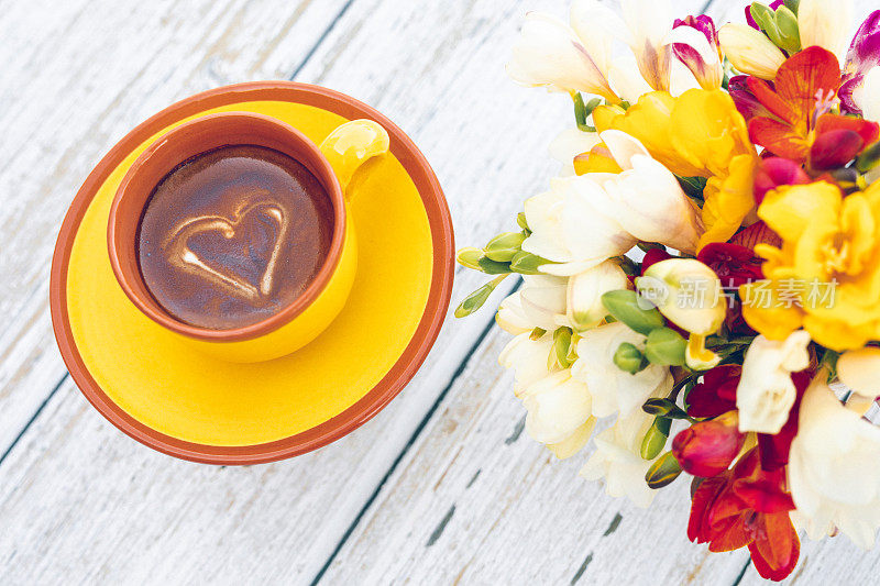 黄色杯，波西米亚风格的奶油咖啡，小苍兰和一个爱心形状的咖啡
