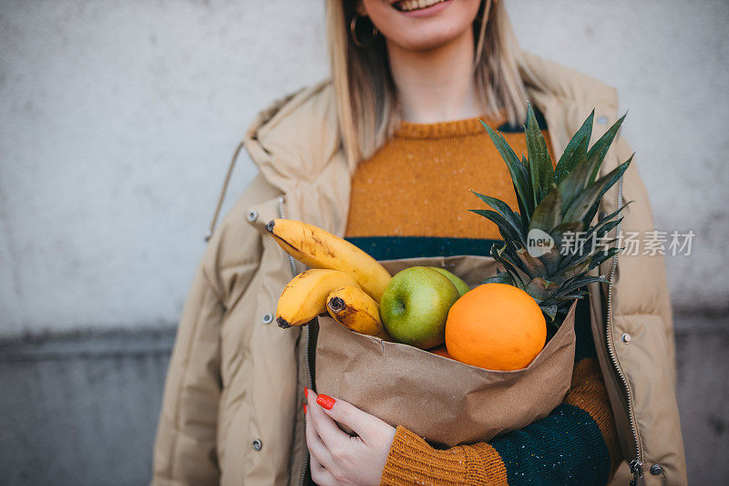 一个年轻的女人拿着一个装着新鲜水果的纸袋