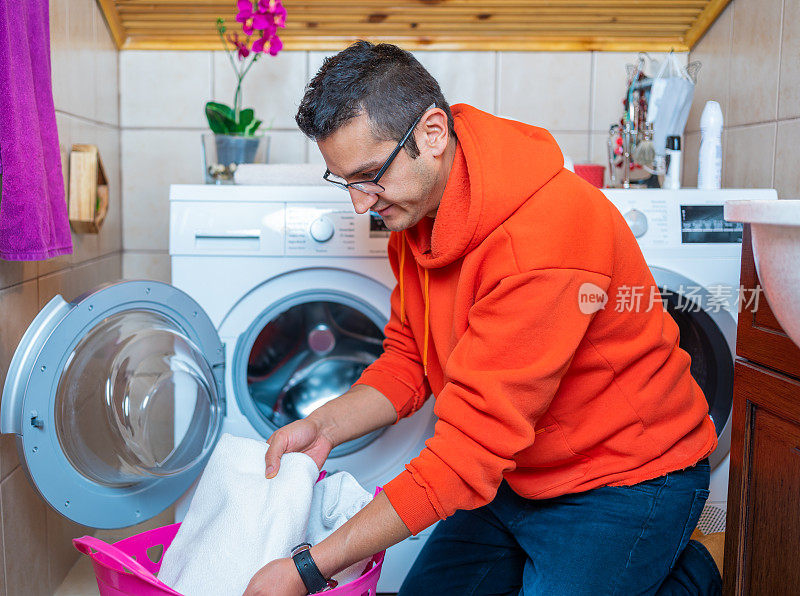 一个年轻人正在把衣服放进浴室的洗衣机里。洗衣日