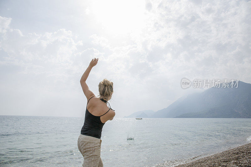 年轻女子早上从海滩上扔石头