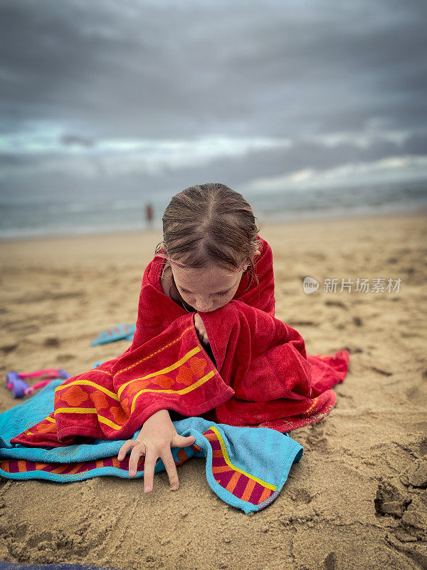 孩子们裹着红毛巾坐在海滩上