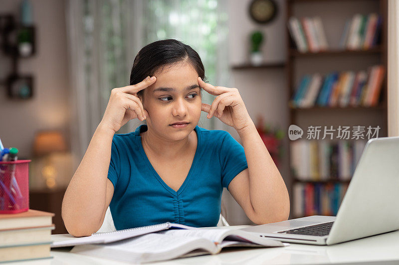 一个十几岁的女孩在家里学习的照片:-库存照片