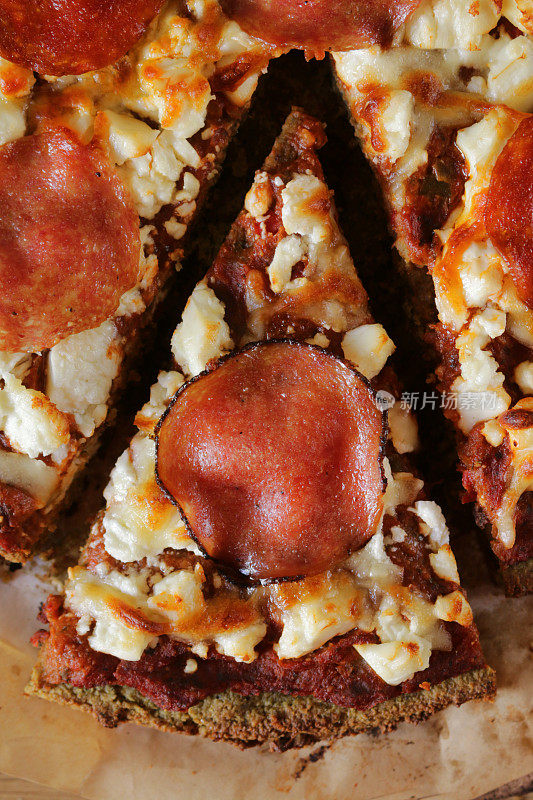 特写镜头:切片的，新鲜烘焙的自制意大利辣香肠披萨，融化的羊乳酪，丰富的番茄番茄沙司和意大利腊肠圈，西兰花的基础上，俯瞰