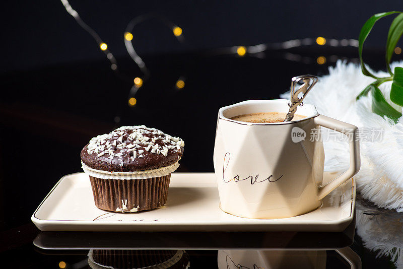 巧克力松饼纸杯蛋糕，椰片和一大杯咖啡或茶在黑色背景