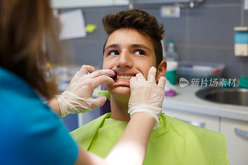 当牙医检查他的牙齿时，男孩坐在牙科椅上。