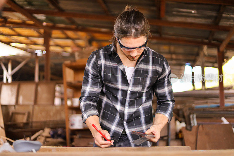 一个白人木匠正在用实心方形测量来衡量他自己的车库风格的车间的木板的爱好