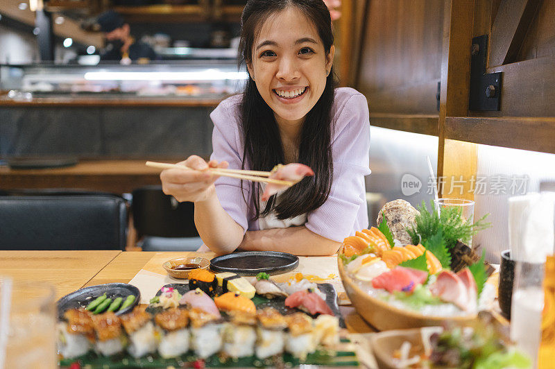 年轻的亚洲女子在一家日本餐厅吃着新鲜的寿司配菜和绿茶