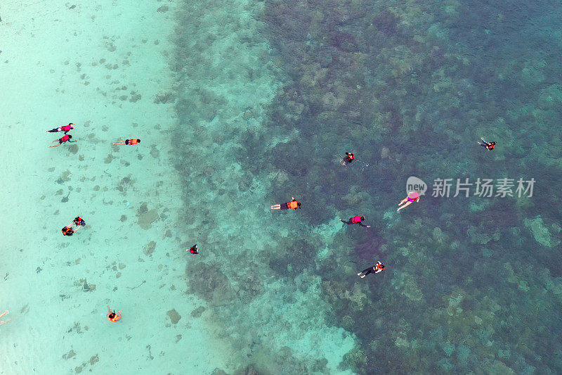 无人机俯视图，人们浮潜在珊瑚礁与清澈的蓝色蓝绿色海水。游客们在珊瑚礁之间透明的海水中游泳。马来西亚的汀吉岛或汀吉岛