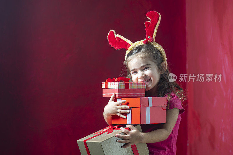 可爱的小女孩戴着圣诞驯鹿的鹿角，手里拿着礼盒