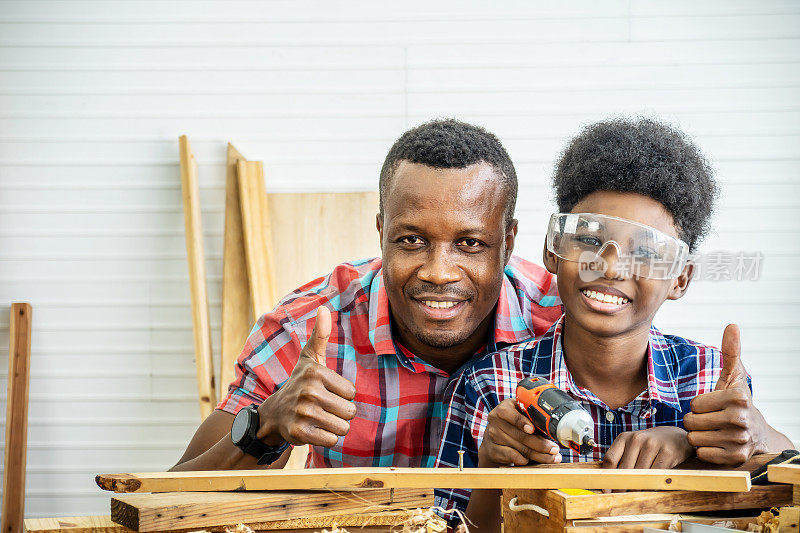 家庭，木工，木工，欢快的非裔美国父亲和小儿子在车间竖起大拇指的画像，上面放着各种工作工具