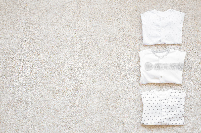 折叠的新生儿紧身衣在浅色的地毯背景上。婴儿衣服。特写镜头。文本的空白位置。自顶向下的观点。