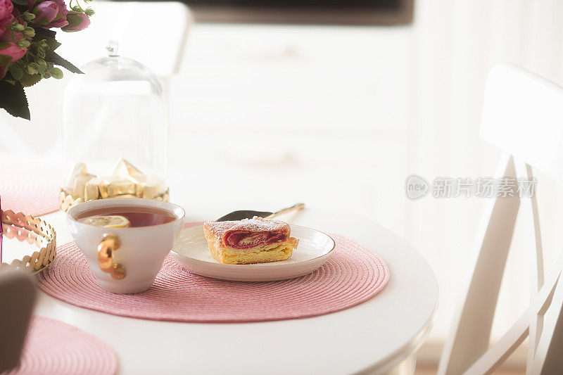 白色桌子上的粉色餐巾纸上有新鲜浆果、鲜花和一杯茶。传统的开胃菜或早餐。斯堪的纳维亚式菜肴和梗类犬。