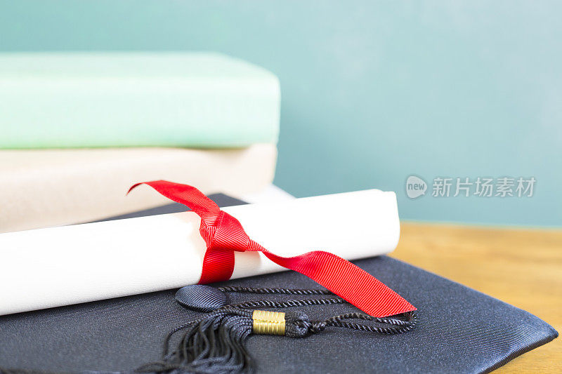 粉笔板背景与学位帽，教科书和文凭在一个抛光的木桌。绝佳的复印空间。