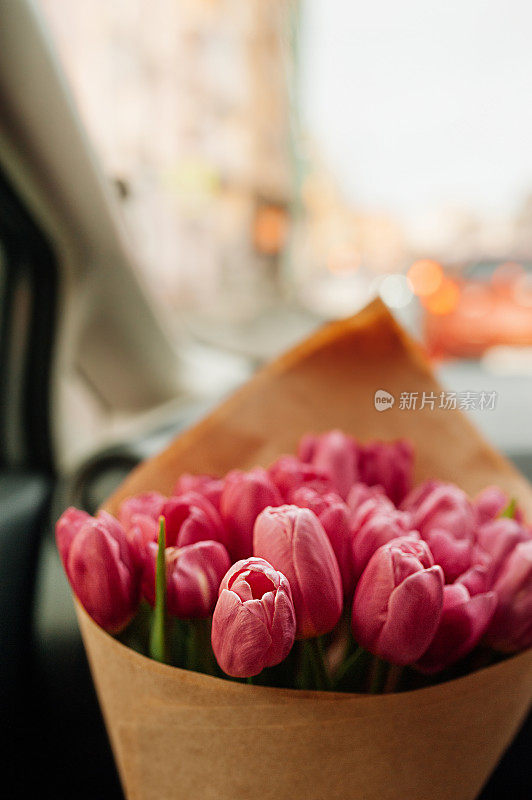 别致的一大束粉红色郁金香用牛皮纸包装在汽车内饰的道路上。花的内容，花的传递，选择性的焦点