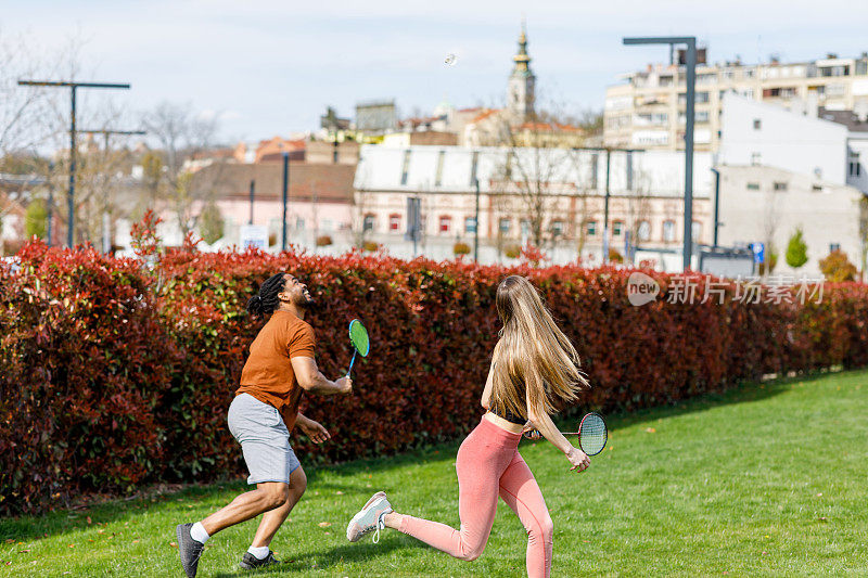幸福的多种族夫妇在公园里打羽毛球。