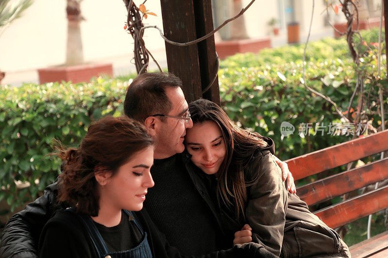 特写肖像的父亲和两个年轻的成年女儿坐在公园的长凳