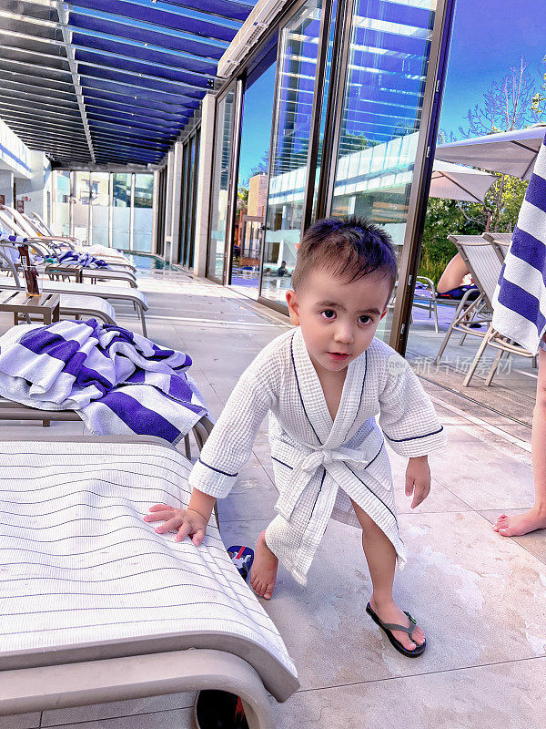 小男孩穿着浴袍从泳池里出来。