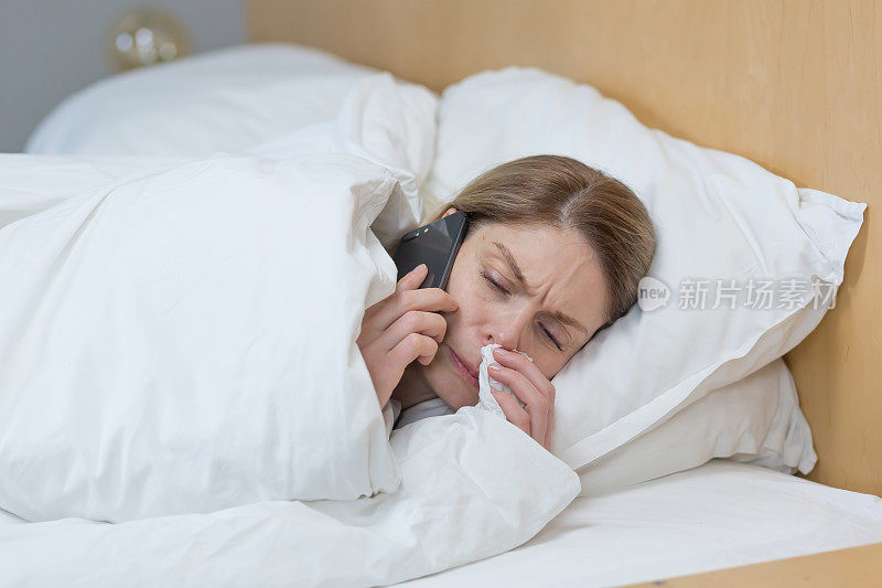 一个生病的女人在家里的特写照片，有一个糟糕的流鼻涕和感冒，躺在床上盖着毯子，打电话给医生建议