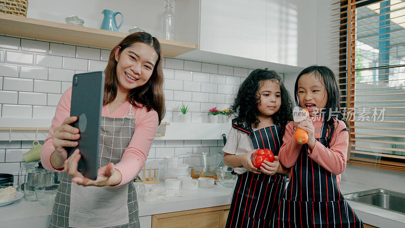 年轻的亚洲母亲在与女儿在家做饭时接到丈夫的视频电话。