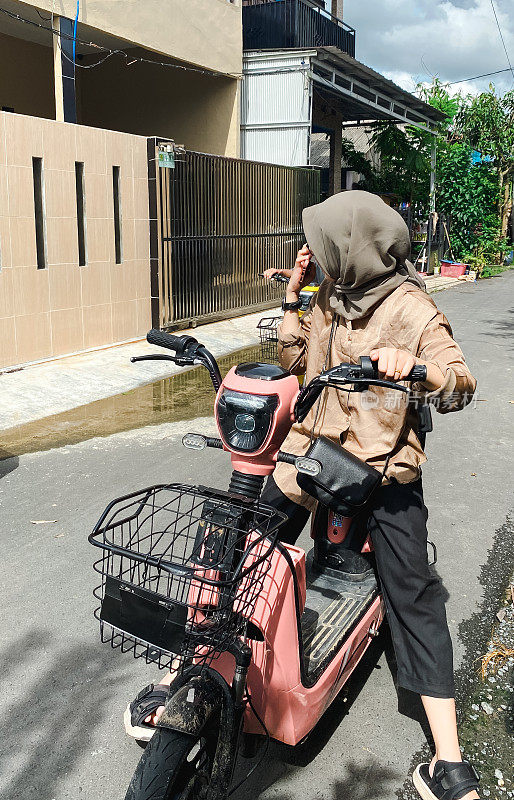 年轻的伊斯兰妇女在居民区骑电动自行车