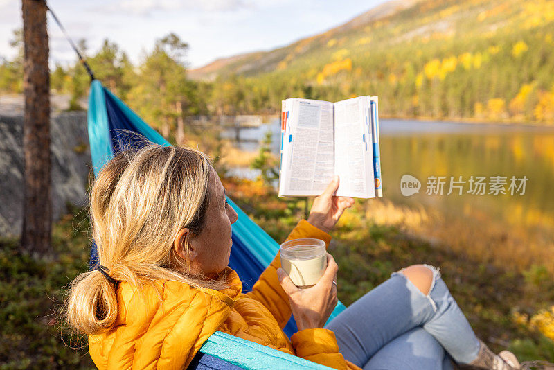 一个女人躺在湖边的吊床上，看书，喝茶，露营