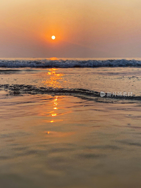 美丽的海边橙色日落日出映照在大海和潮湿的沙滩上，温柔的海浪在海岸上破碎，潮汐反射涟漪，太阳落在海滩上