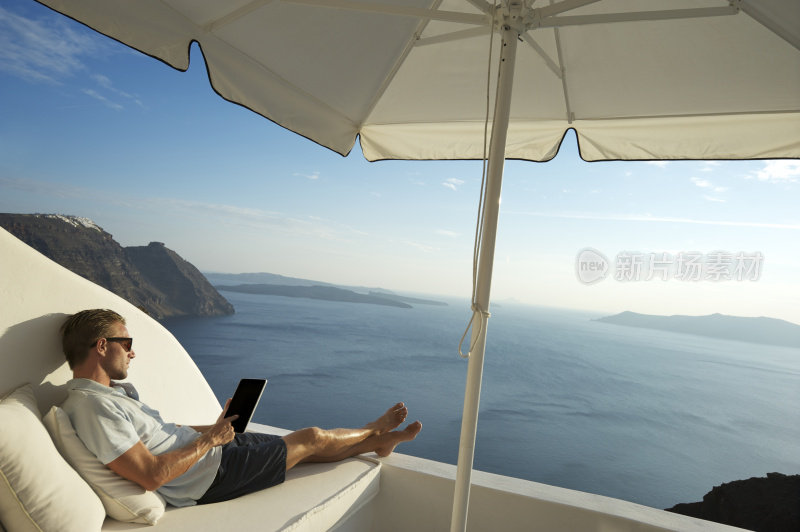 一个年轻人在海边的阳台上用平板电脑放松